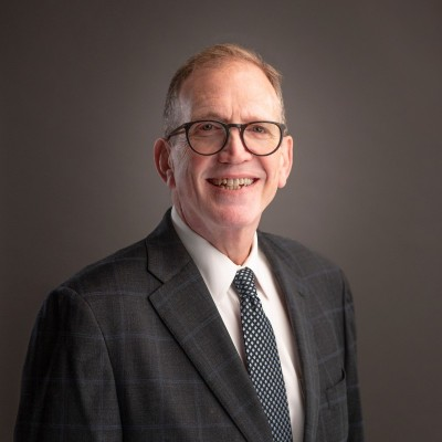 Picture of Steven Snyder, Former VP at East Boston Neighborhood Health Center. Professional portrait of a smiling man with glasses wearing a suit and tie against a gray background.