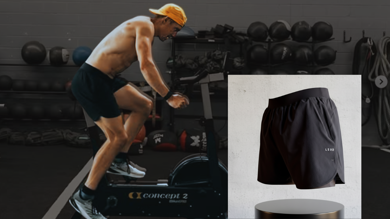 A shirtless man wearing black shorts and a yellow cap is riding a stationary exercise bike in a gym. The gym has black medicine balls, weights, and ropes. An inset shows a close-up of black athletic shorts with a small white logo that reads 'LSXD.'