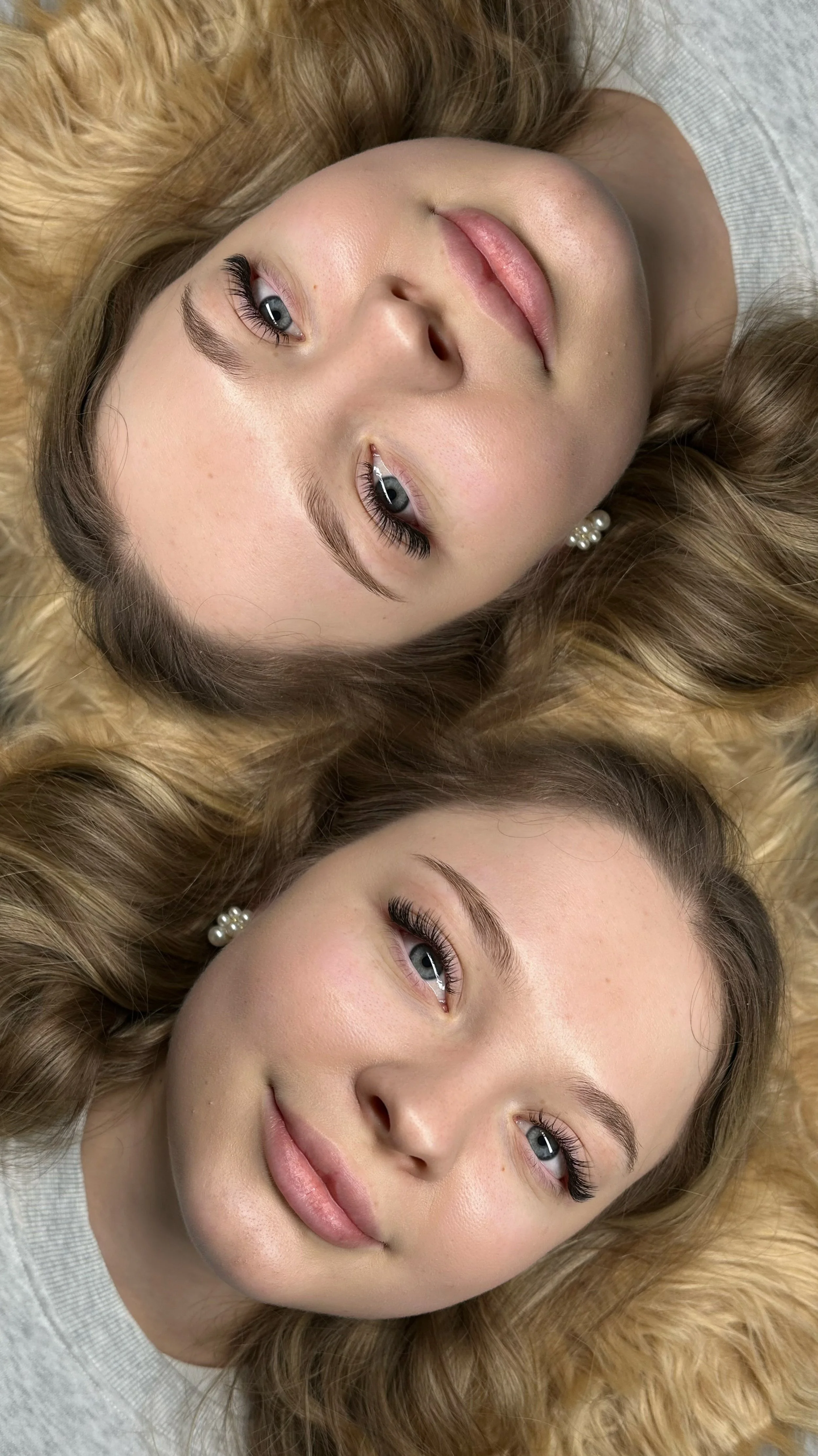 Two similar-looking women lying side by side with their heads on a light-colored surface, facing opposite directions.