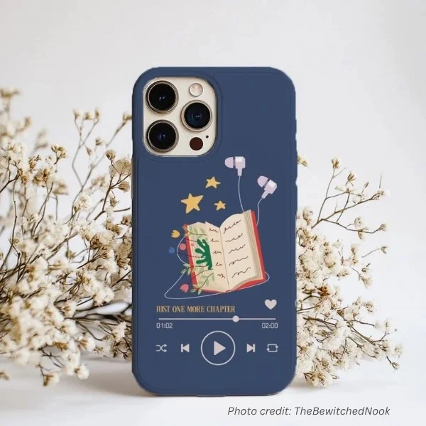 'Just One More Chapter' phone case by TheBewitchedNook. Displays a book, earphones and the 'play' menu.