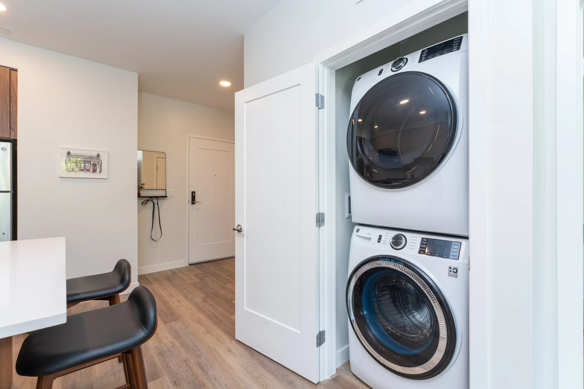Stacked white washer and dryer inside a closet with an open door, in a modern home interior