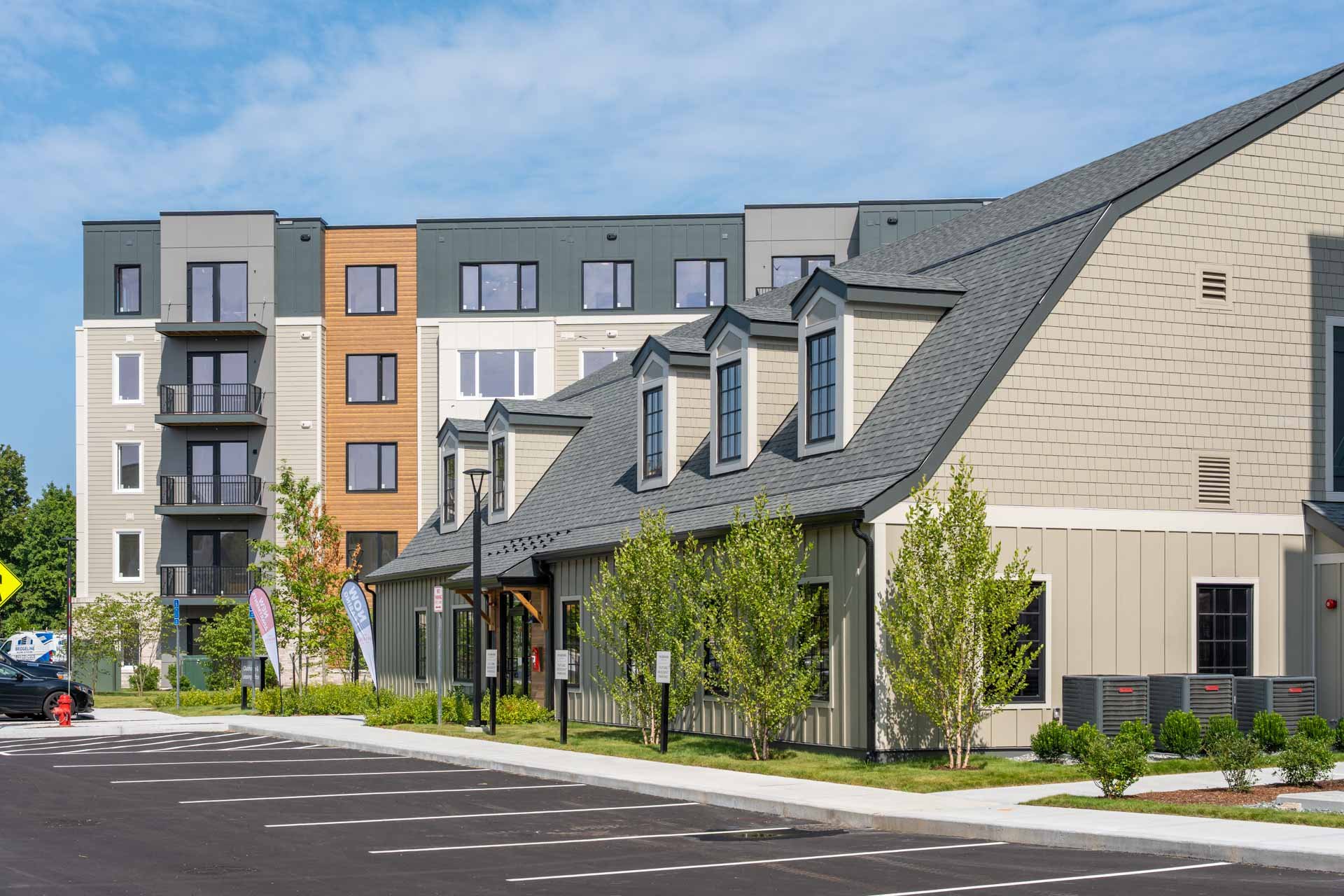 The Devon at Weiss Farm clubhouse and leasing center parking lot in the foreground, trees and streetlights, blue sky.