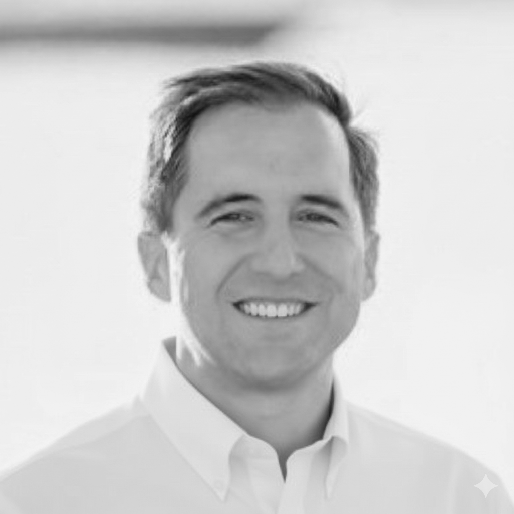 Black and white photo of a smiling man with short hair wearing a collared shirt.
