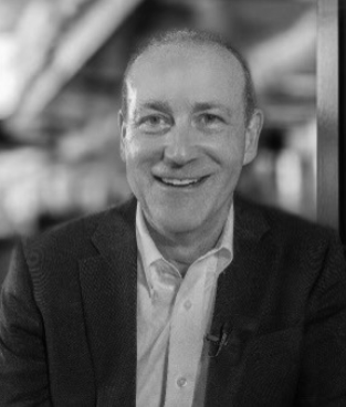 A smiling man in a suit jacket and white shirt, in a black and white photo.