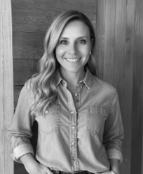 Black and white photo of a smiling woman with long wavy hair, wearing a denim button-up shirt.