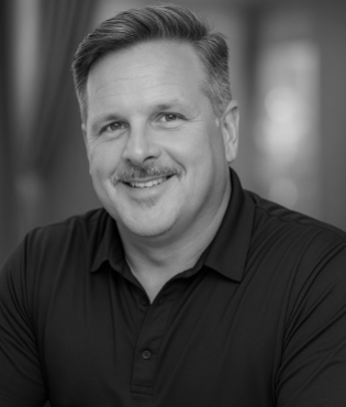 Black and white portrait of a smiling man with short hair and a mustache, wearing a collared shirt.