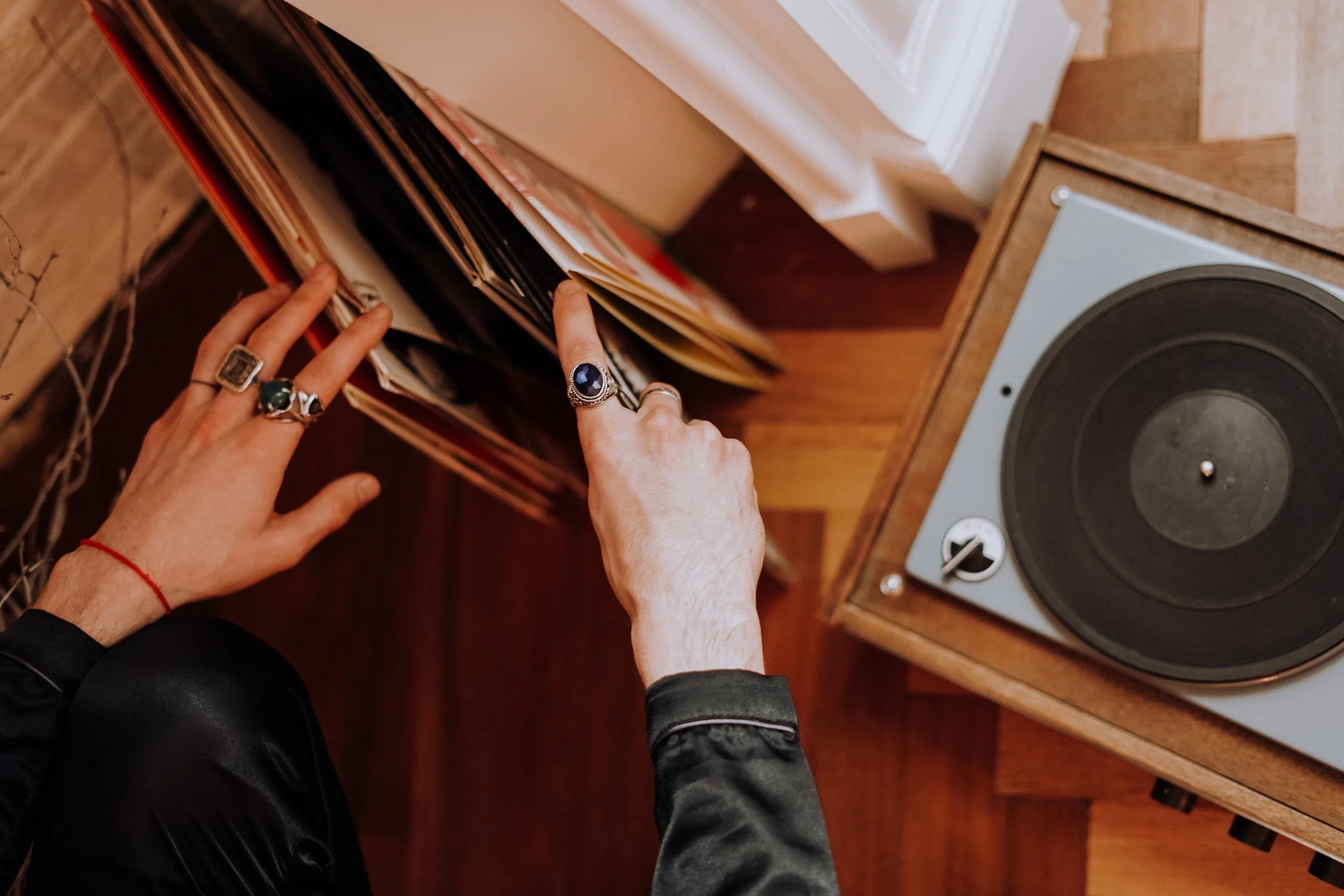 Person flipping through vinyl records in a wooden storage unit in a room with wooden flooring, next to a turntable.