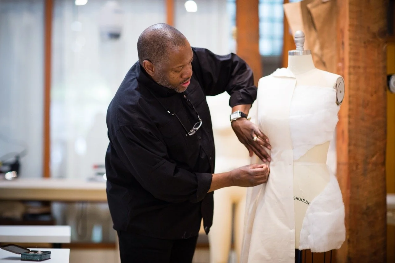 A man working on a dress form in a workshop, adjusting fabric on a mannequin.