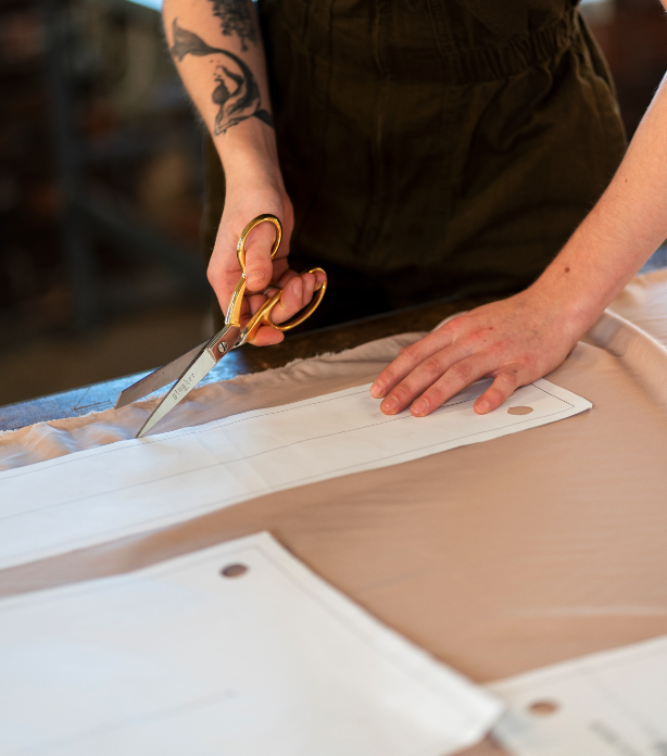 Person cutting fabric with gold-handled scissors on worktable.