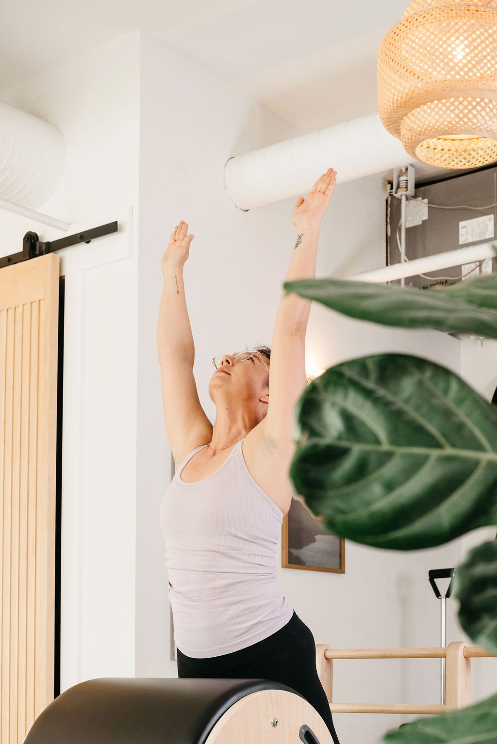 A woman stretching with her arms raised above her head in a bright, modern room.