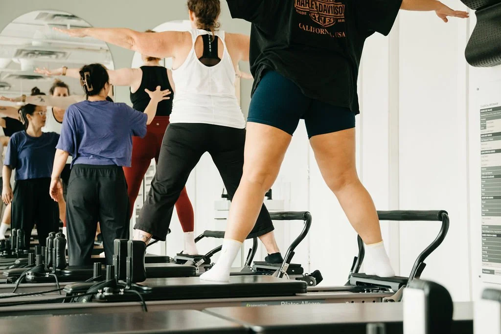 Multiple women exercising on Pilates reformer machines in a fitness studio.