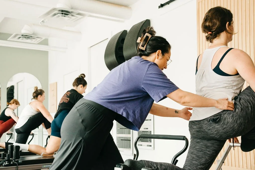 A fitness instructor assisting a woman with stretching exercises during a workout class in a gym.