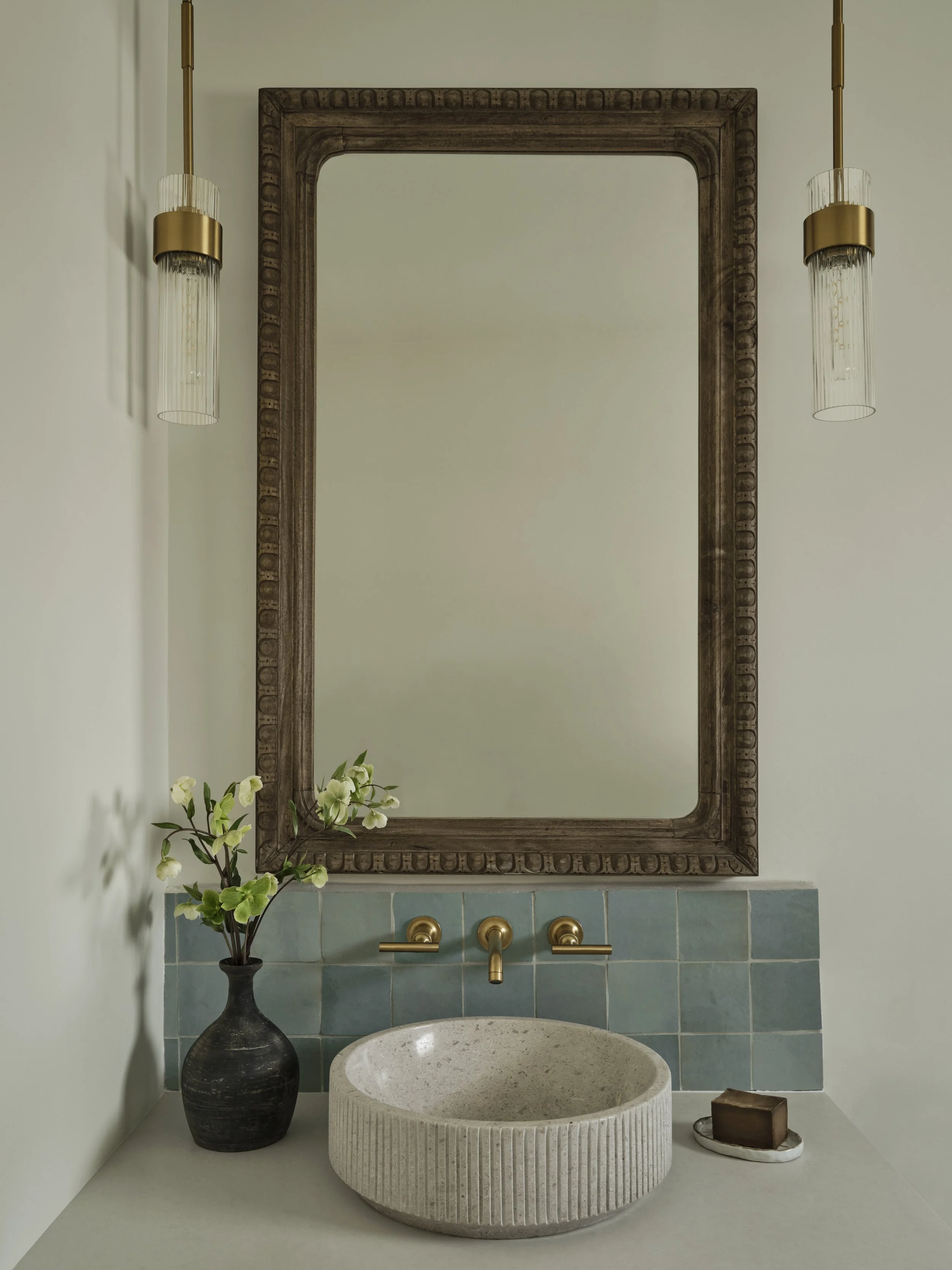Santa Barbara luxury powder room design with carved wood mirror, blue zellige tile, fluted stone vessel sink, and brass fixtures.