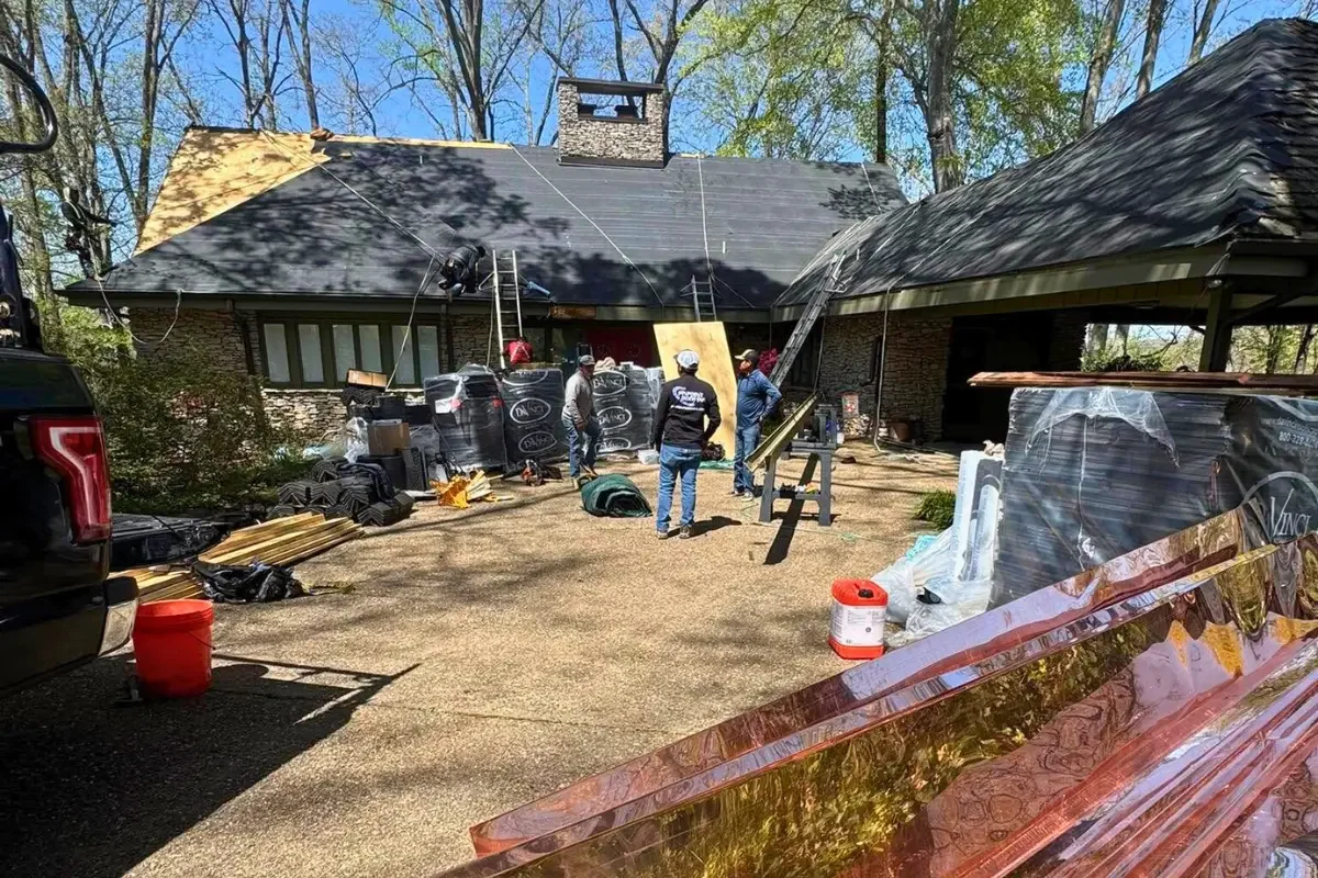 View of a house roof with new a roof crew prepping the shop and making roof repairs.  There are piles of materials and supplies in the foreground.
