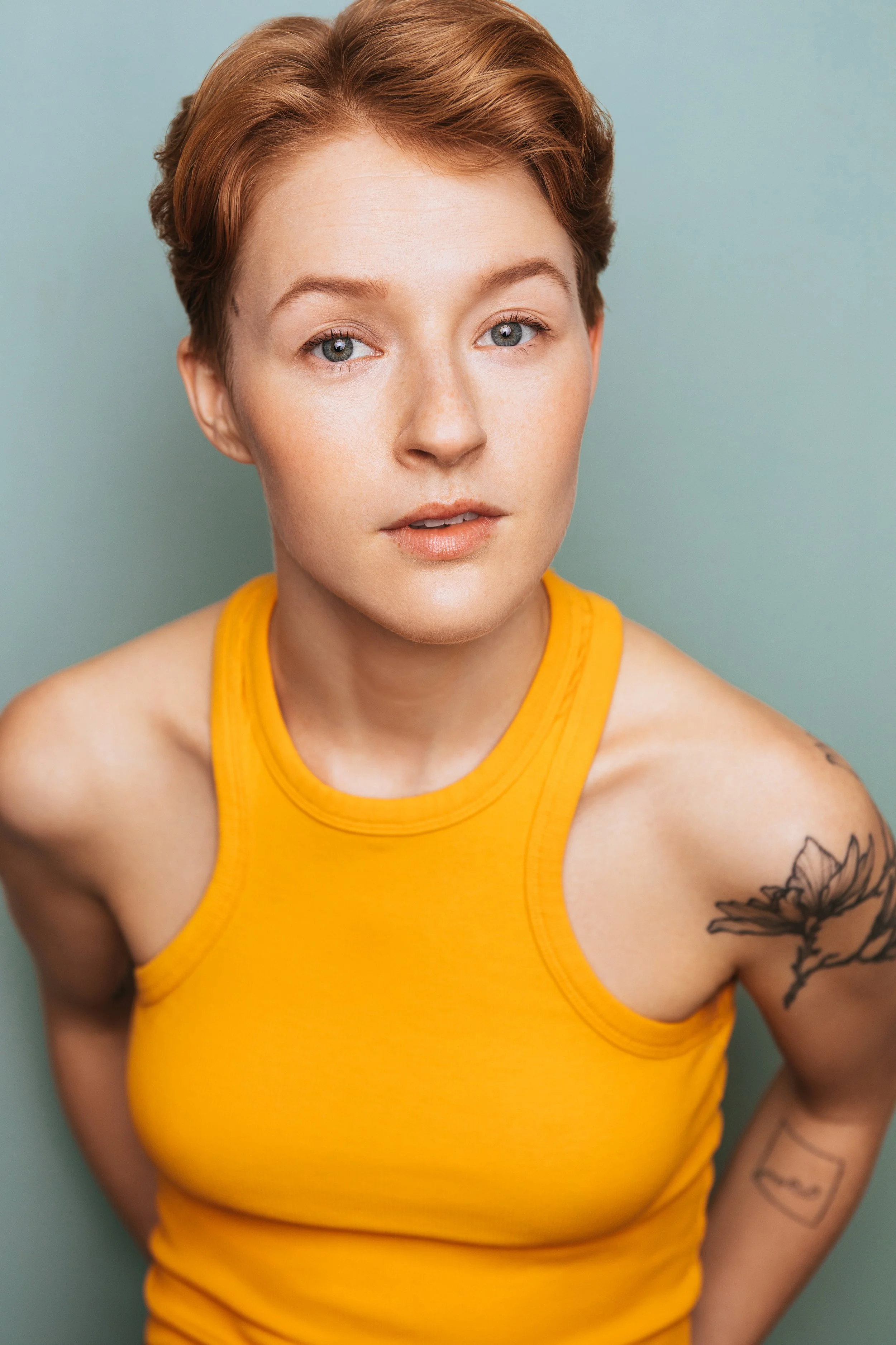 Hawley Gould in an orange tank, magnolia tattoo visible on shoulder, leaning in towards camera intently, on a light blue background

by Julianna McGuirl