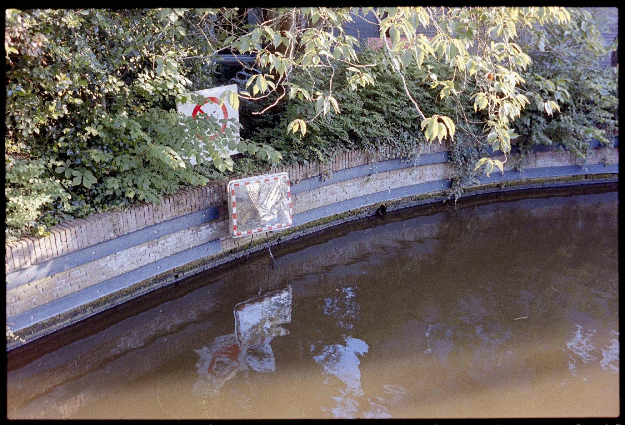 Mirror on a blind corner of the Alkmaar canal, leading to a very low bridge that boaters must lay down to fit under.