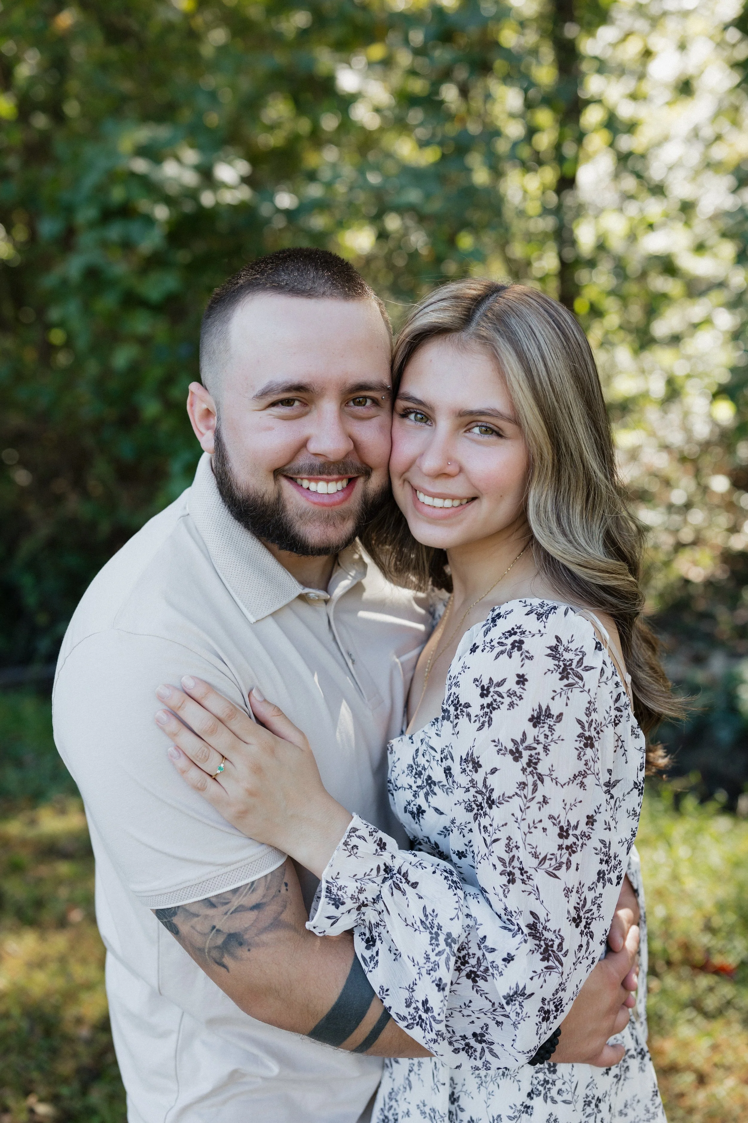A smiling couple embracing outdoors with trees in the background.