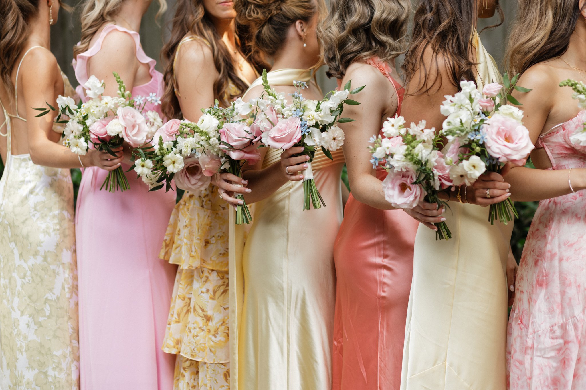Women in colorful dresses holding bouquets of pink and white flowers during a wedding or celebration.