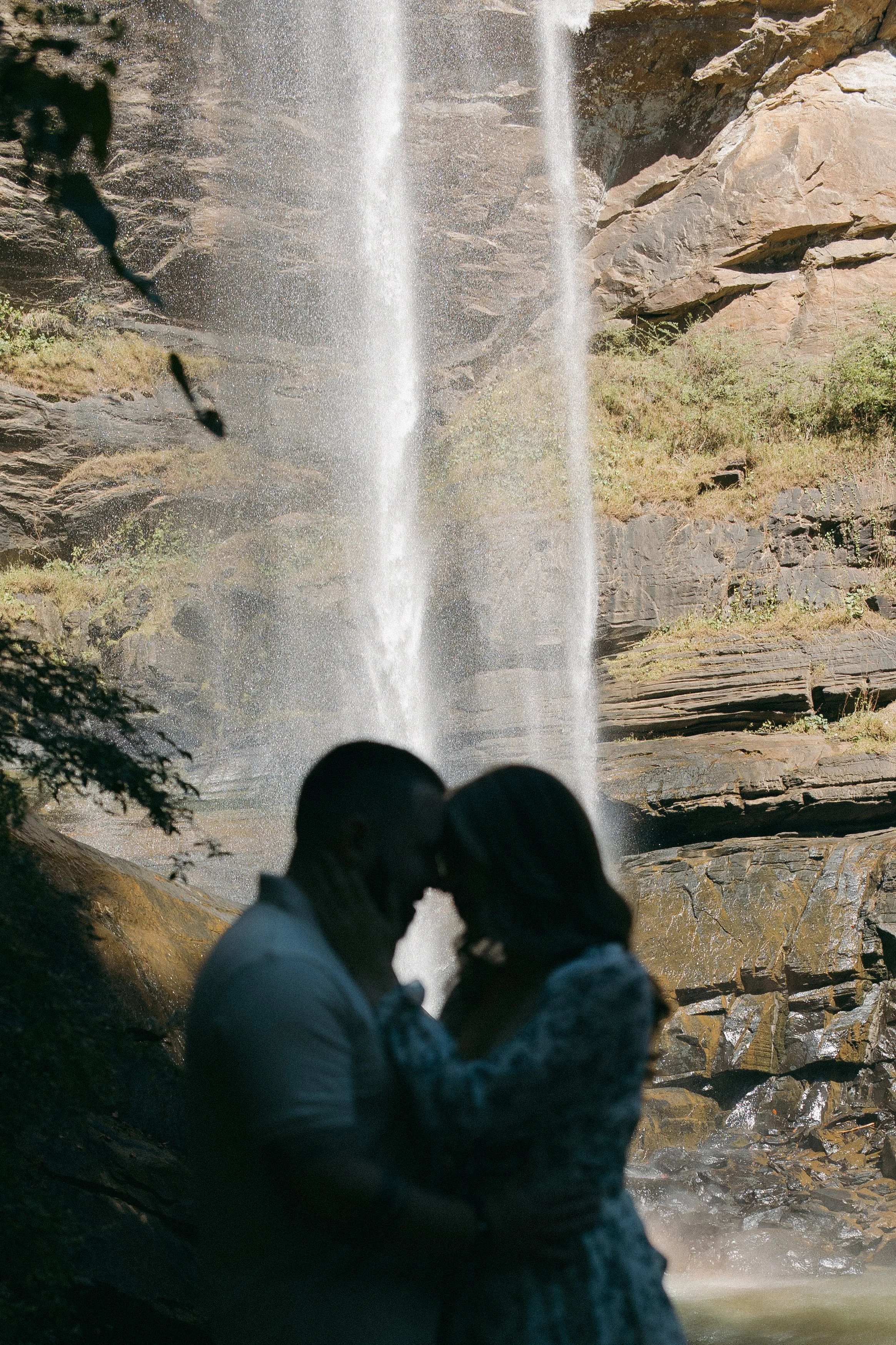 A couple sharing an intimate moment in front of a waterfall.