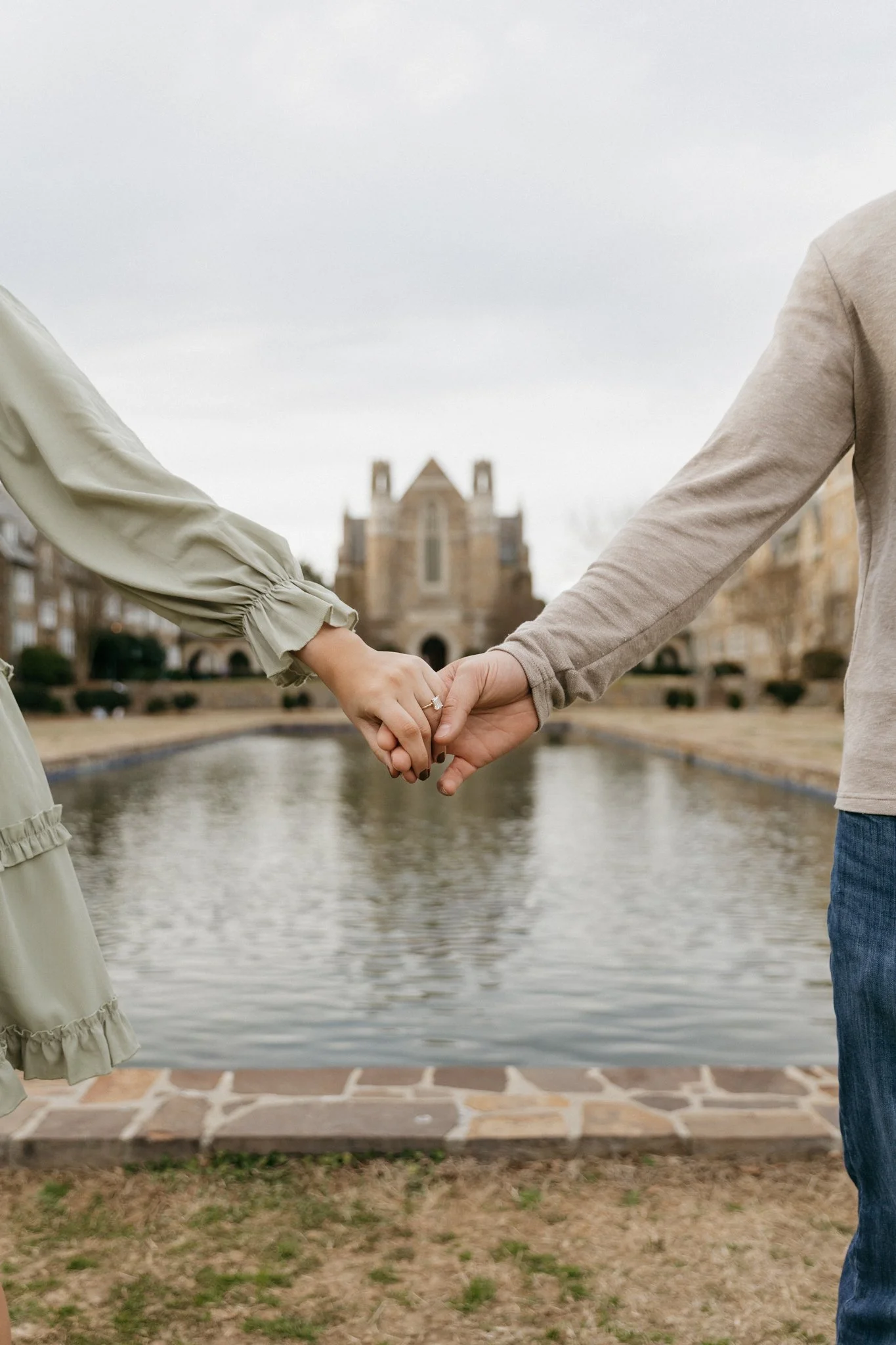 A couple holding hands in front of a canal with a church in the background.