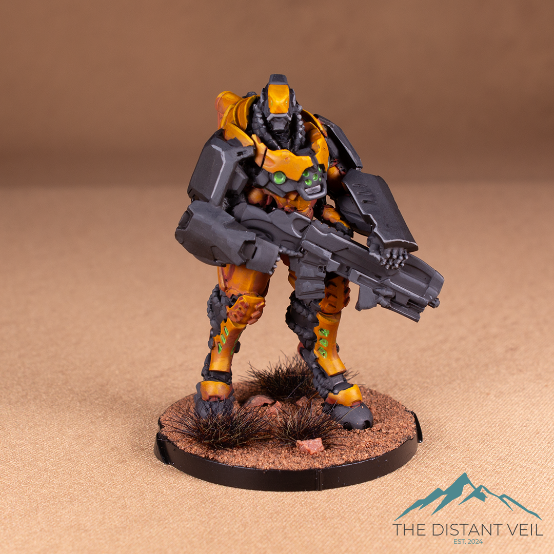 A detailed miniature figure of a sci-fi armored soldier holding a large futuristic rifle, standing on a textured desert base with grass tufts.