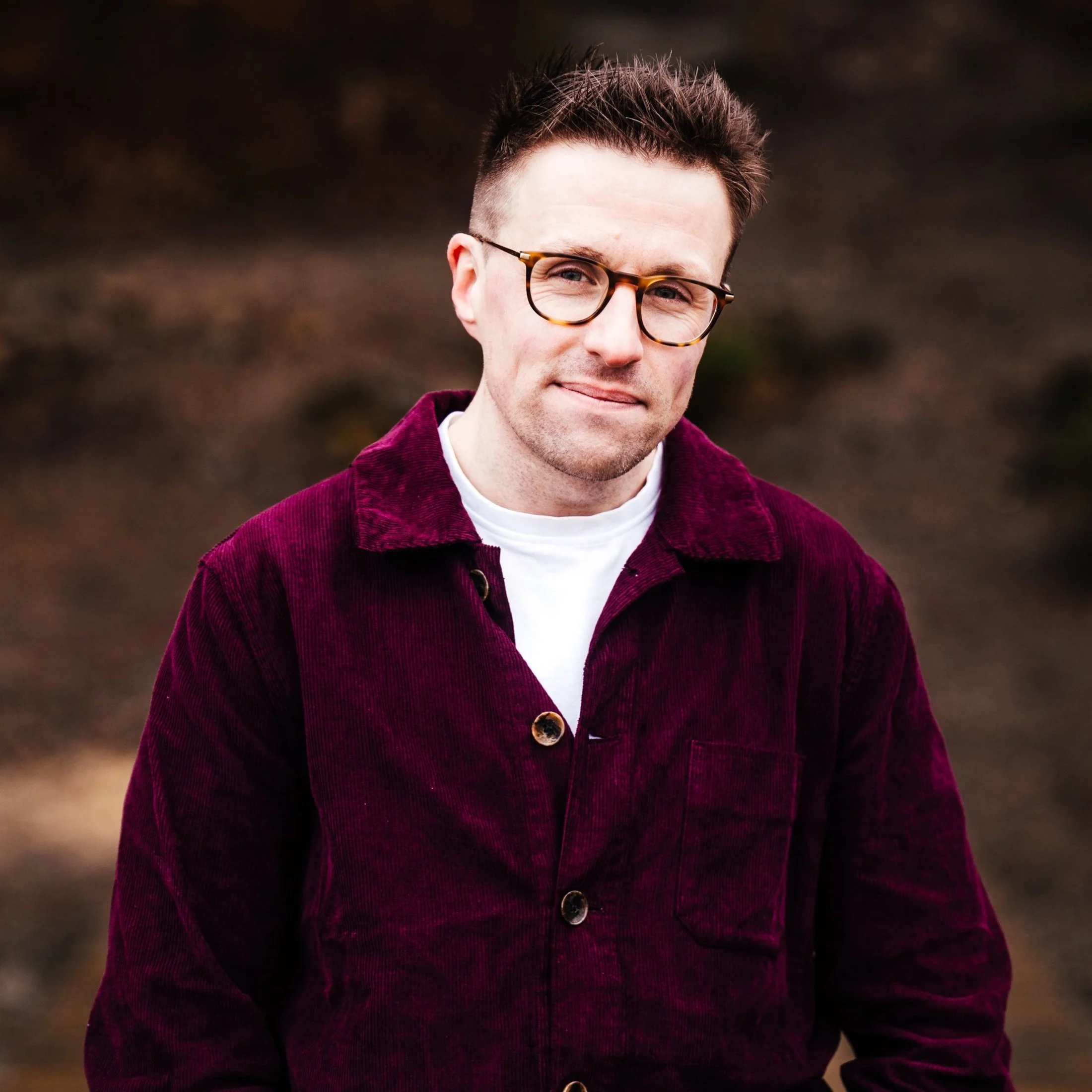 Andy Hunt is wearing glasses and a purple jacket outdoors. He is looking into the camera and smiling.