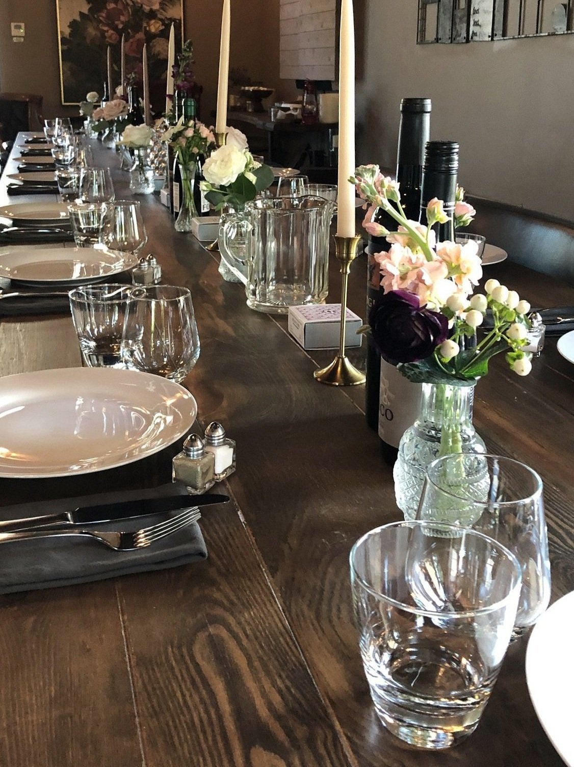 A wooden table with white candles, a black vase with colorful flowers, and a chalkboard sign displaying Wi-Fi credentials.