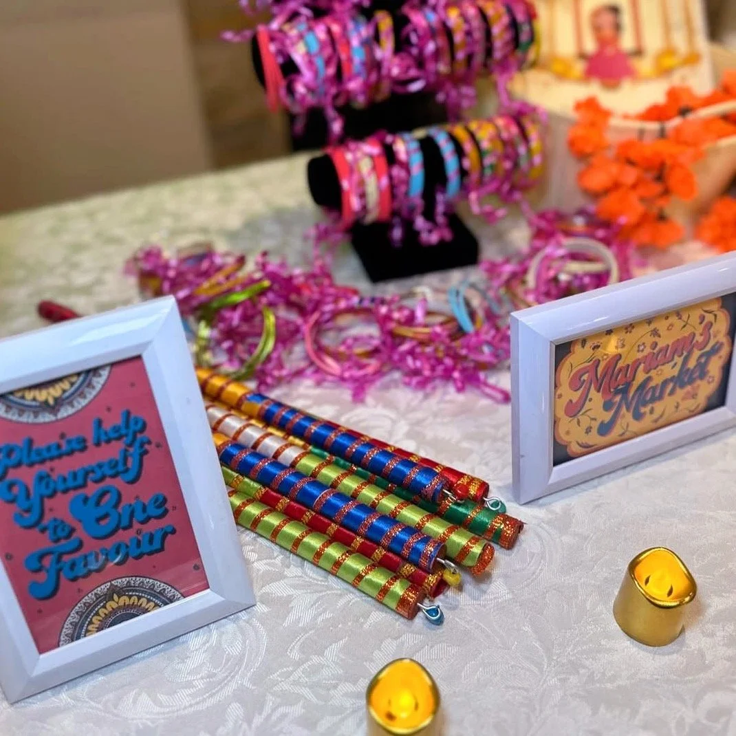 Colourful bangles, flower bracelets and decorative sticks on display at a table for a mehndi wedding event.