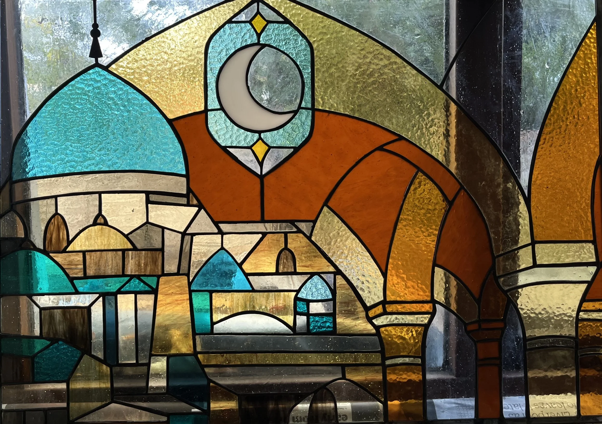 Colorful stained glass window depicting a mosque, a crescent moon, and architectural scene.