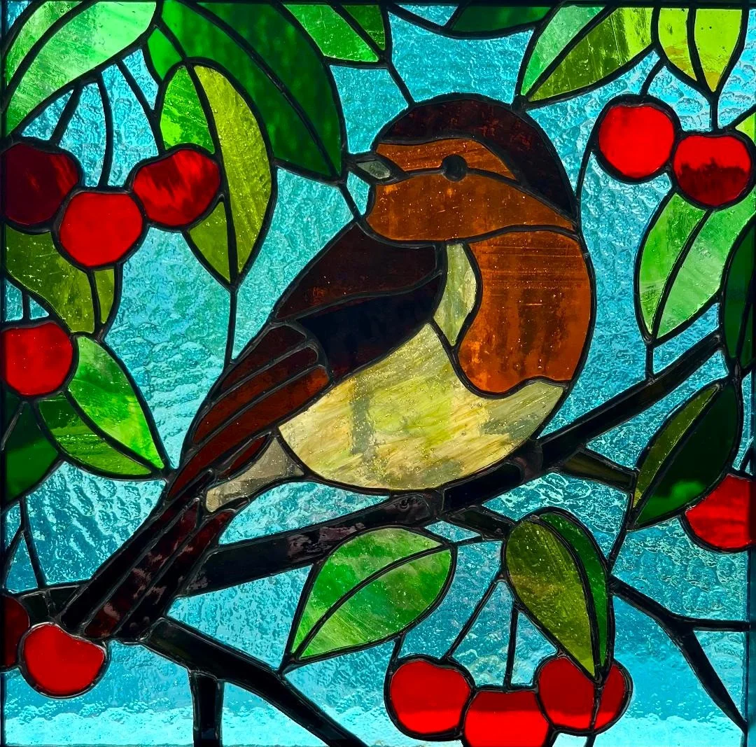 Stained glass window depicting a robin perched on a branch with green leaves and red berries, against a blue background.