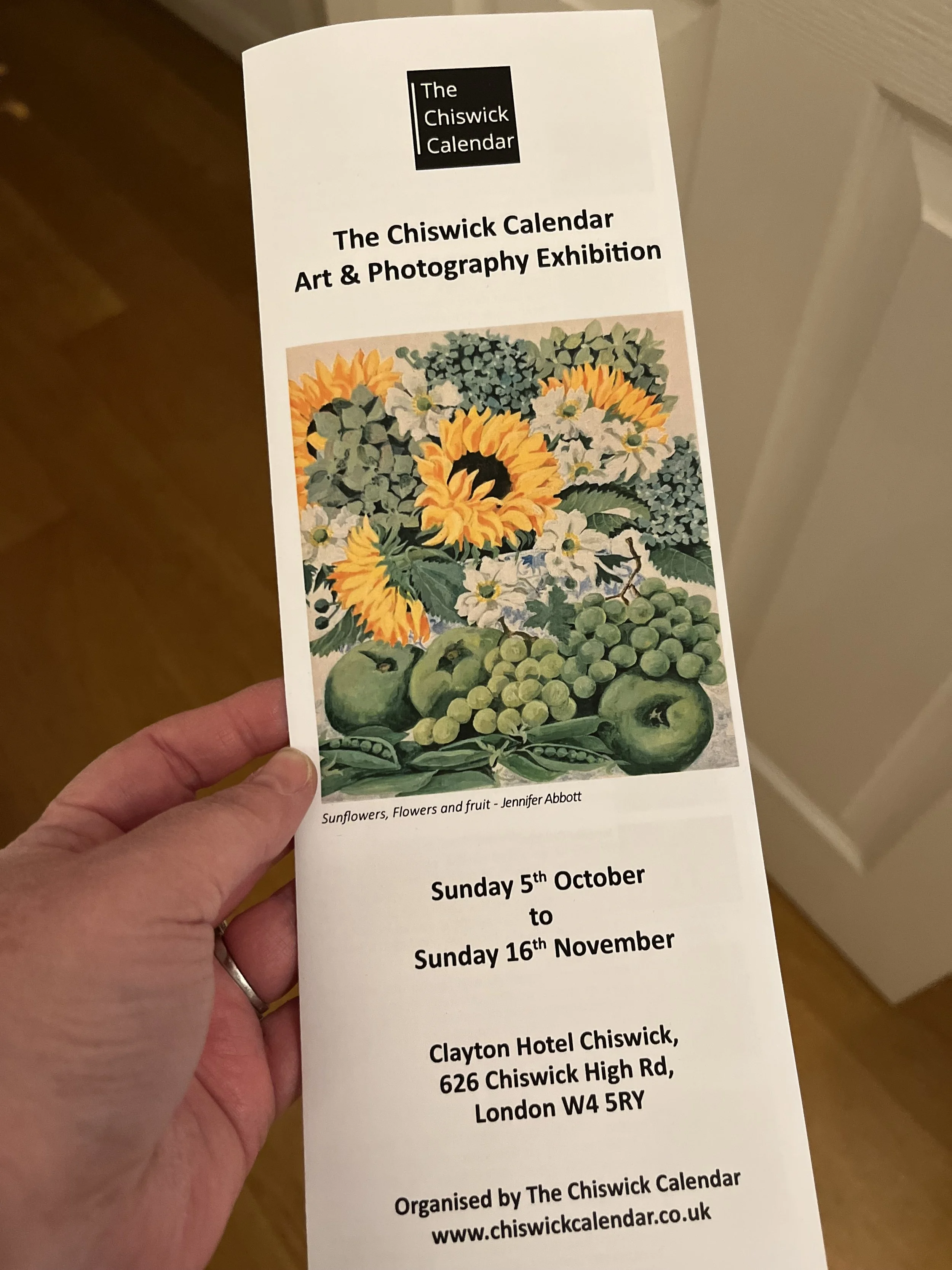 Flyer for The Chiswick Calendar Art & Photography Exhibition, featuring an illustration of sunflowers, flowers, and fruit including apples and grapes, with details of the event dates, location, and organizer.