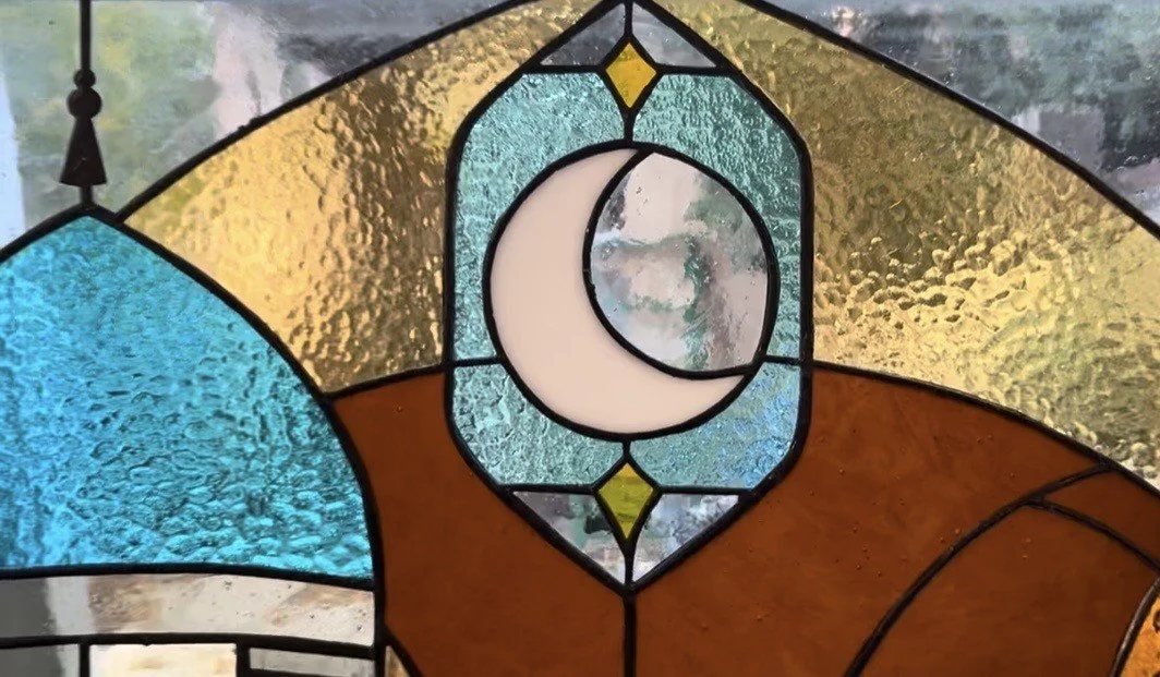 Close-up of a stained glass window with a crescent moon design in the center and textured glass in various colors.