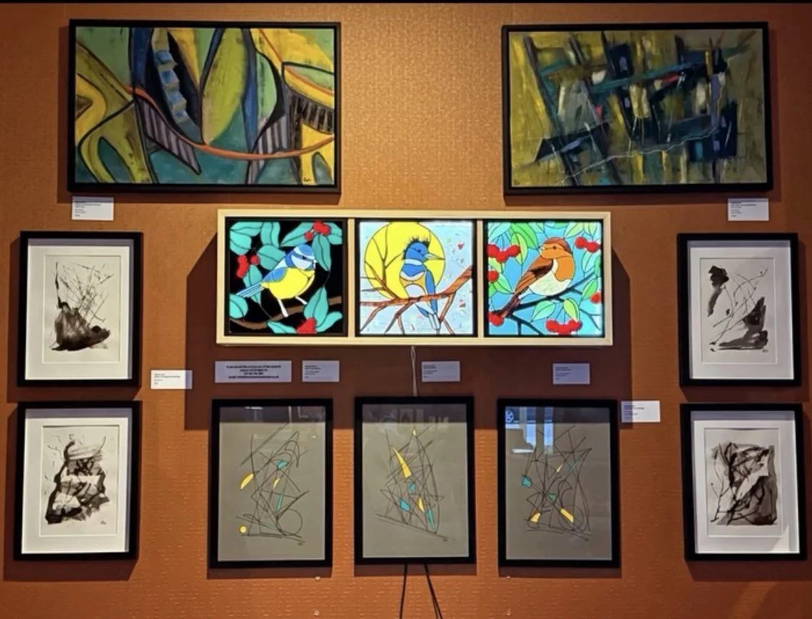 Art gallery display with three stained glass pieces featuring birds and branches.