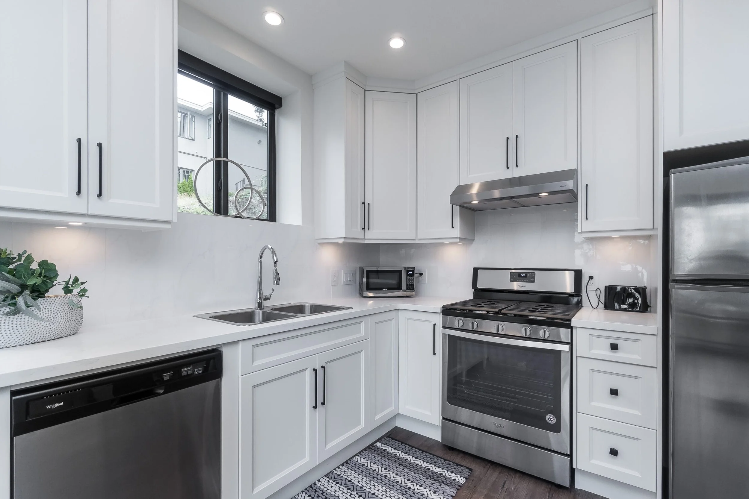 Modern kitchen with white cabinets, stainless steel appliances, double sink, and window above the counter.