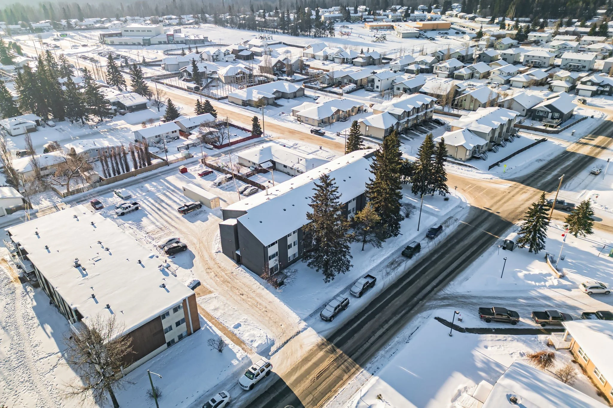 Aerial view of a snow-covered suburban neighborhood with houses, buildings, and streets in a winter landscape.