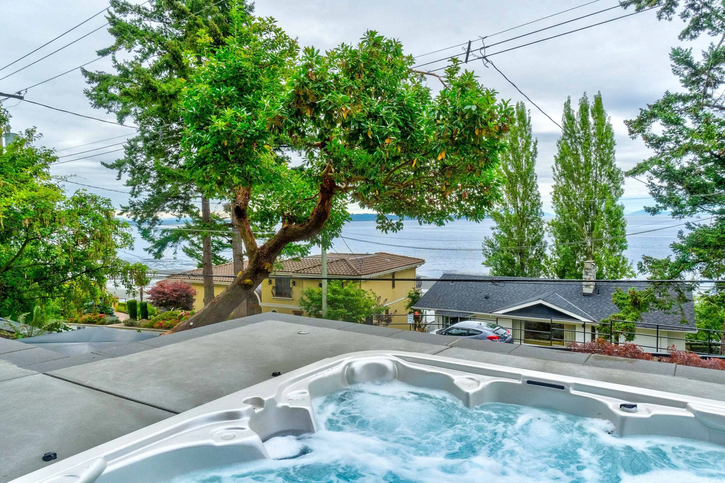 View from a hot tub overlooking houses and a body of water with trees and power lines.
