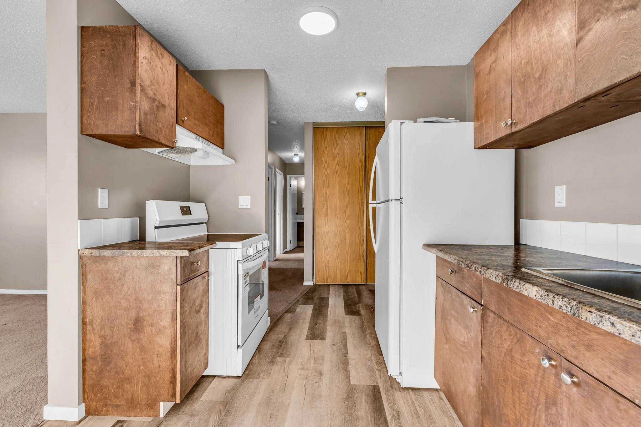 Modern kitchen with wooden cabinets, white appliances, and laminate flooring.