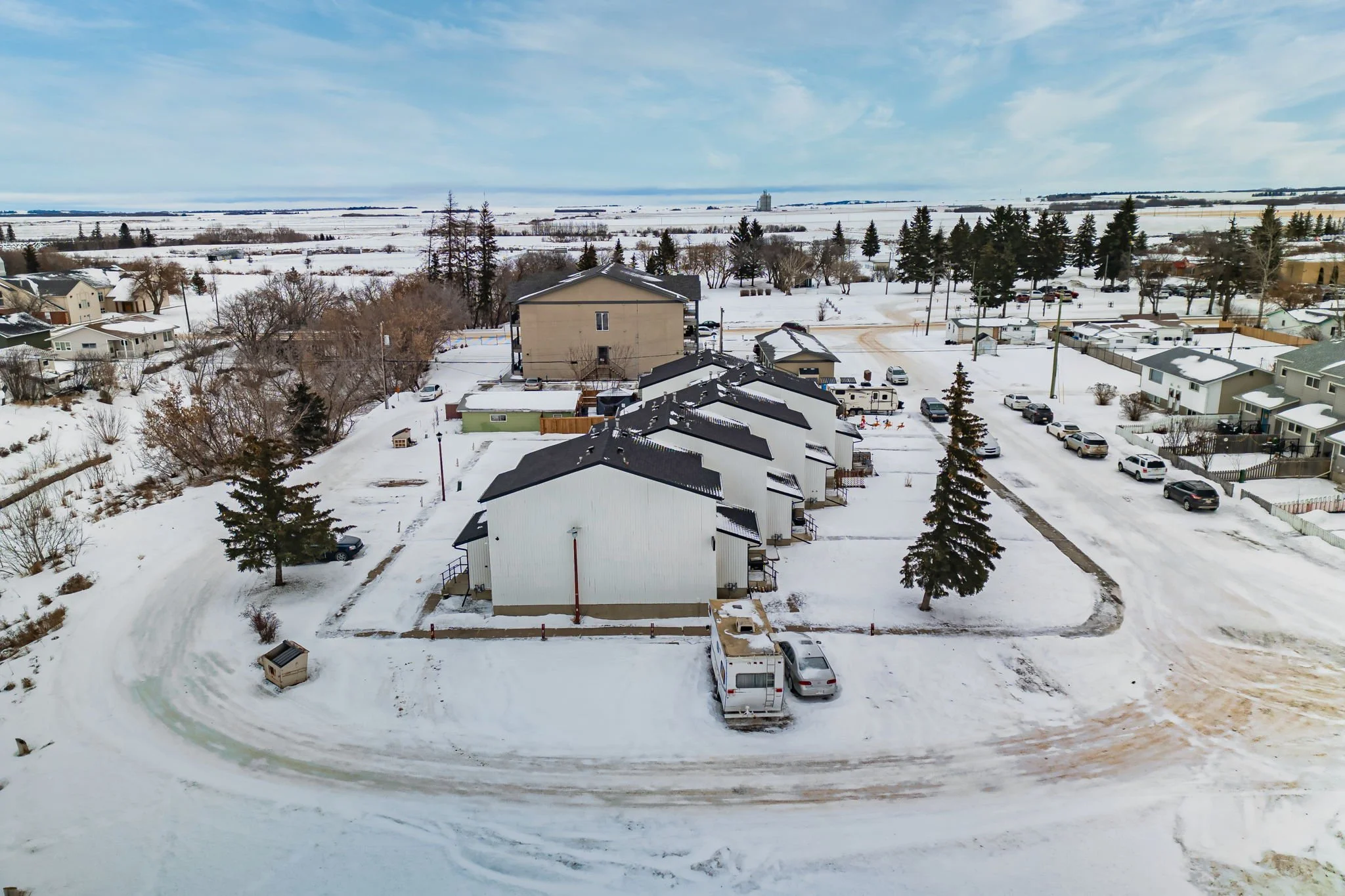 Aerial view of a snowy residential neighborhood with houses, trees, and parked cars.