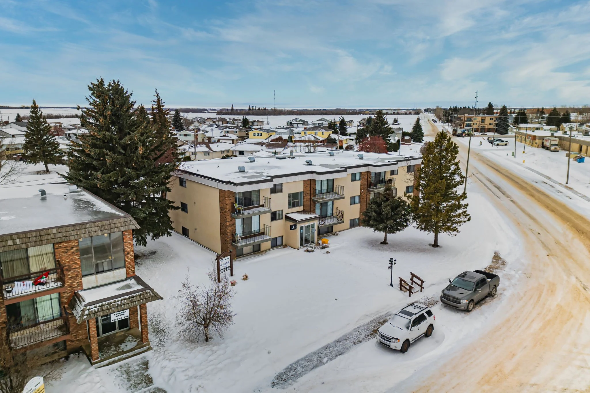 Aerial view of a snowy residential street with an apartment building and parked cars.