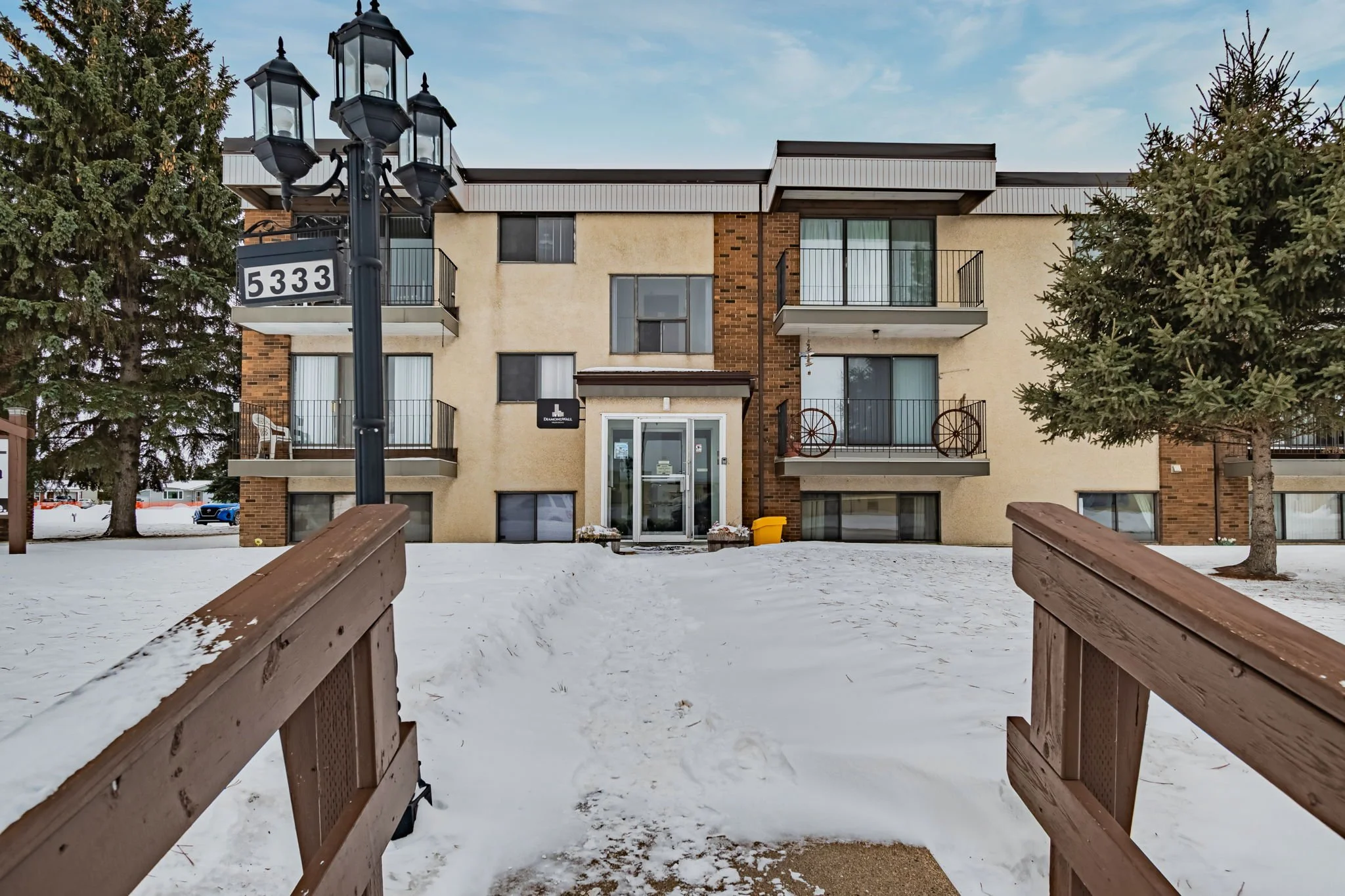 Two-story residential apartment building with balconies, snow-covered ground, and a lamppost displaying the number 5333.