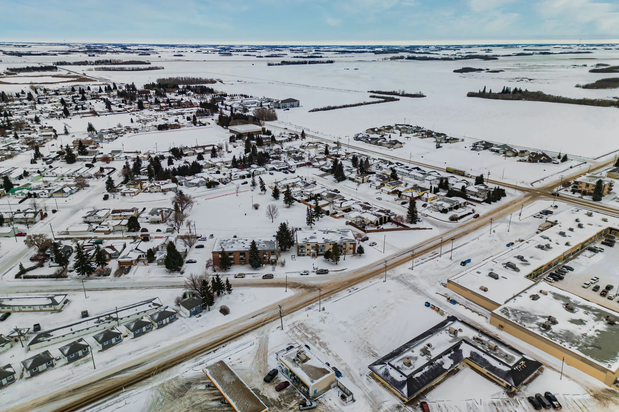 Aerial view of a snow-covered suburban area with residential houses, roads, and a parking lot.