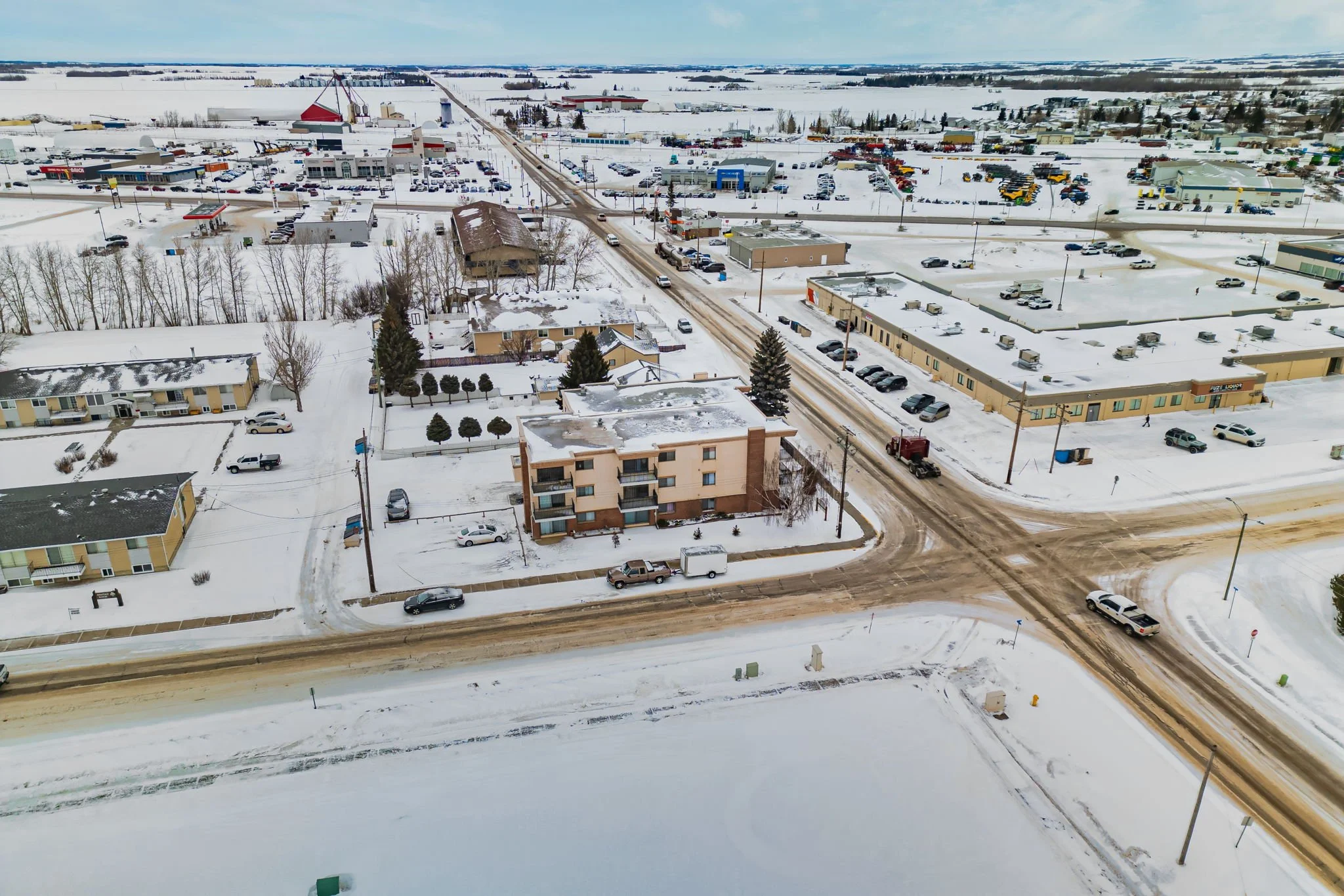 Aerial view of a snow-covered town with roads, buildings, and parked cars.