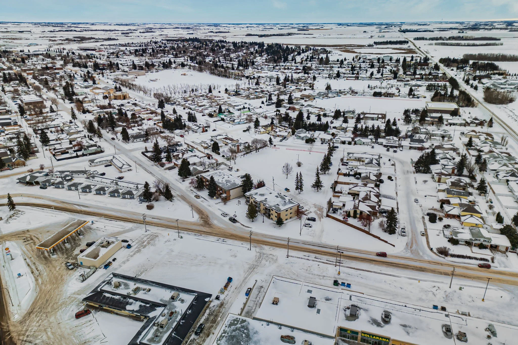 Aerial view of a snow-covered suburban area with houses, roads, and trees in winter.