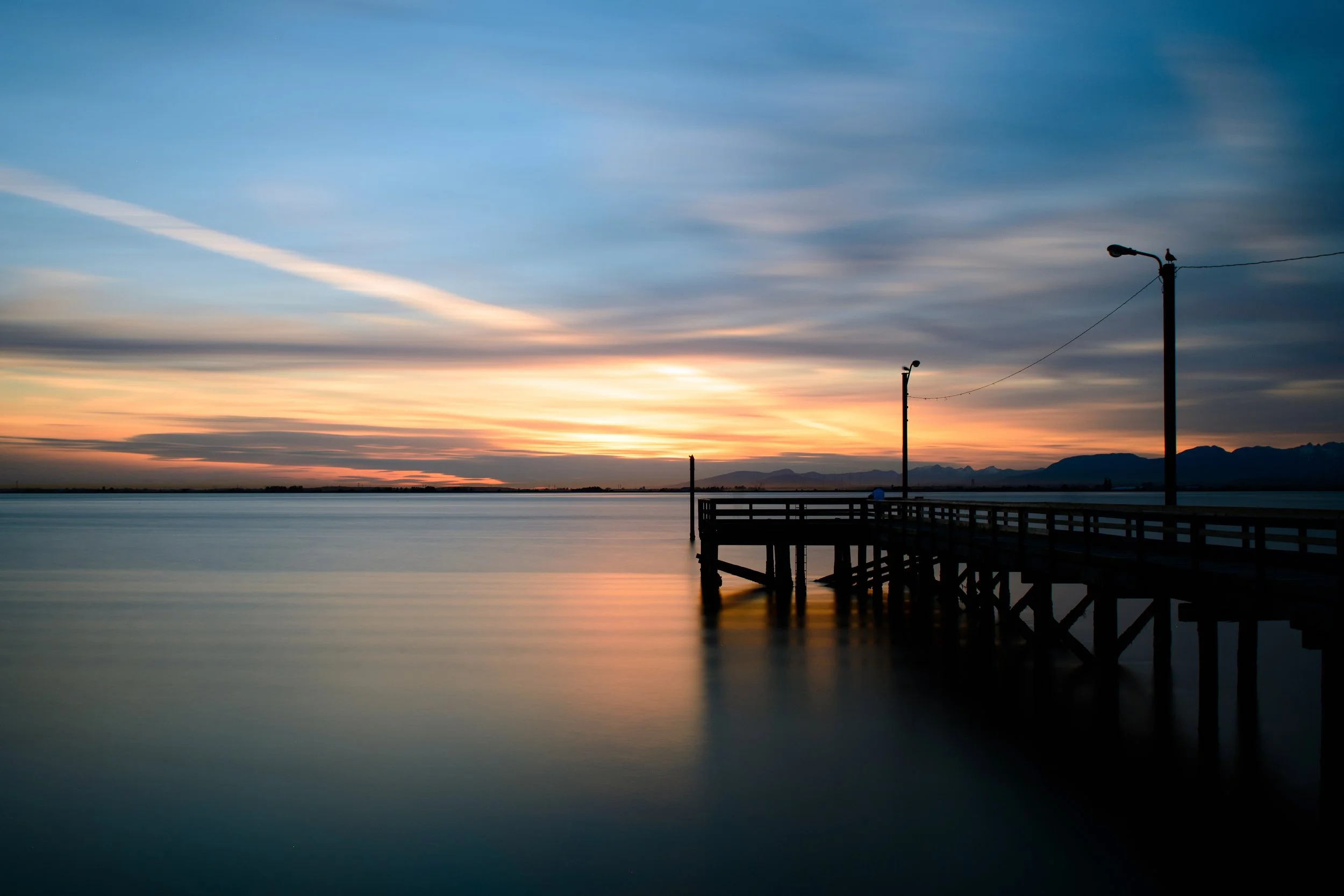 sunset over calm ocean with silhouette of pier and mountains
