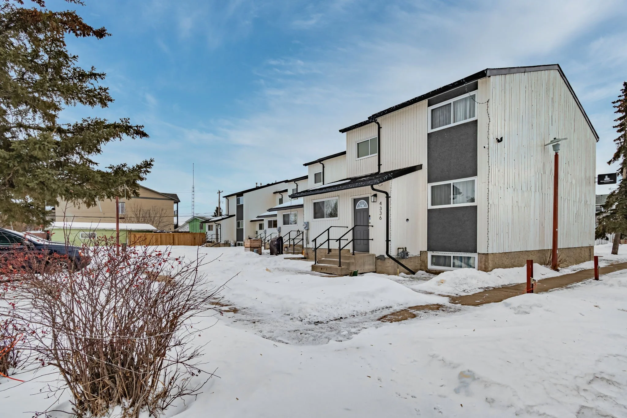 Snow-covered residential area with multiple two-story townhouses, pathway, and bare shrubs under a clear sky.