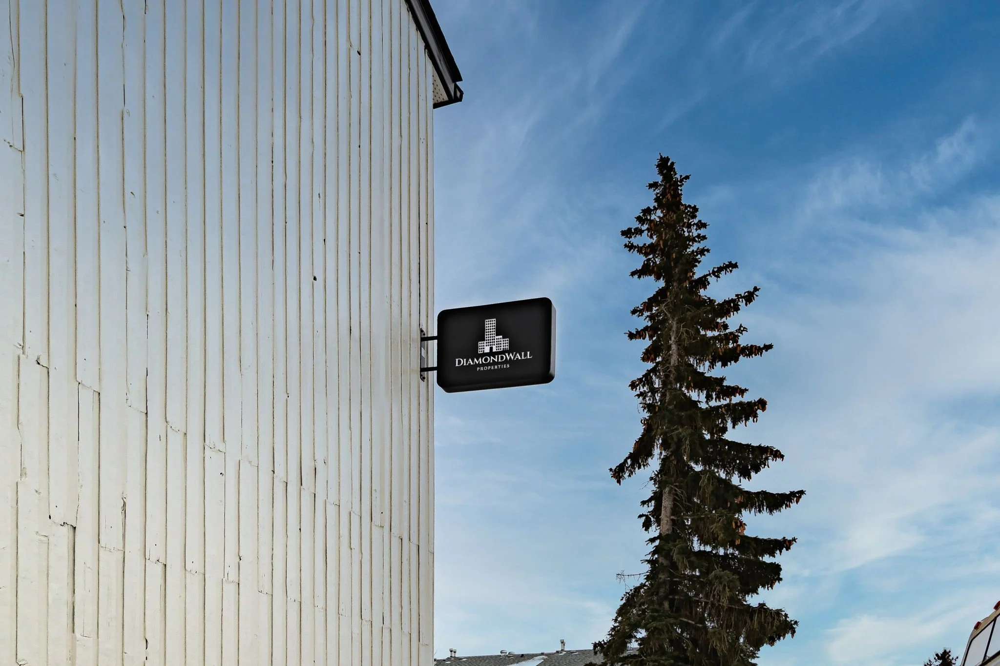 Sign on white building reading 'Diamond Wall Properties' with tree and blue sky
