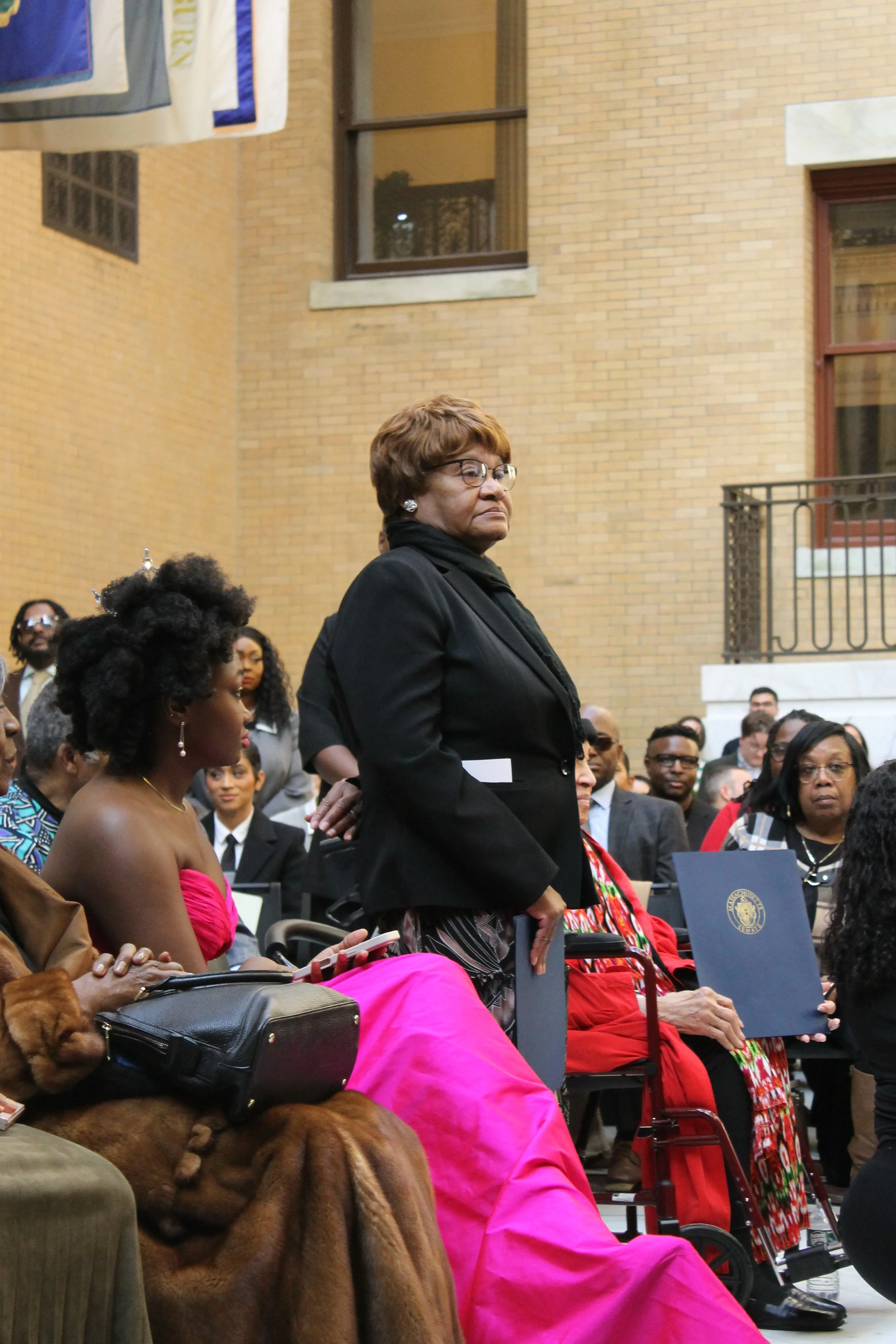 Rev. Mattie Conaway stands to be recognized during the ceremony as attendees look on inside the State House's Great Hall of Flags.