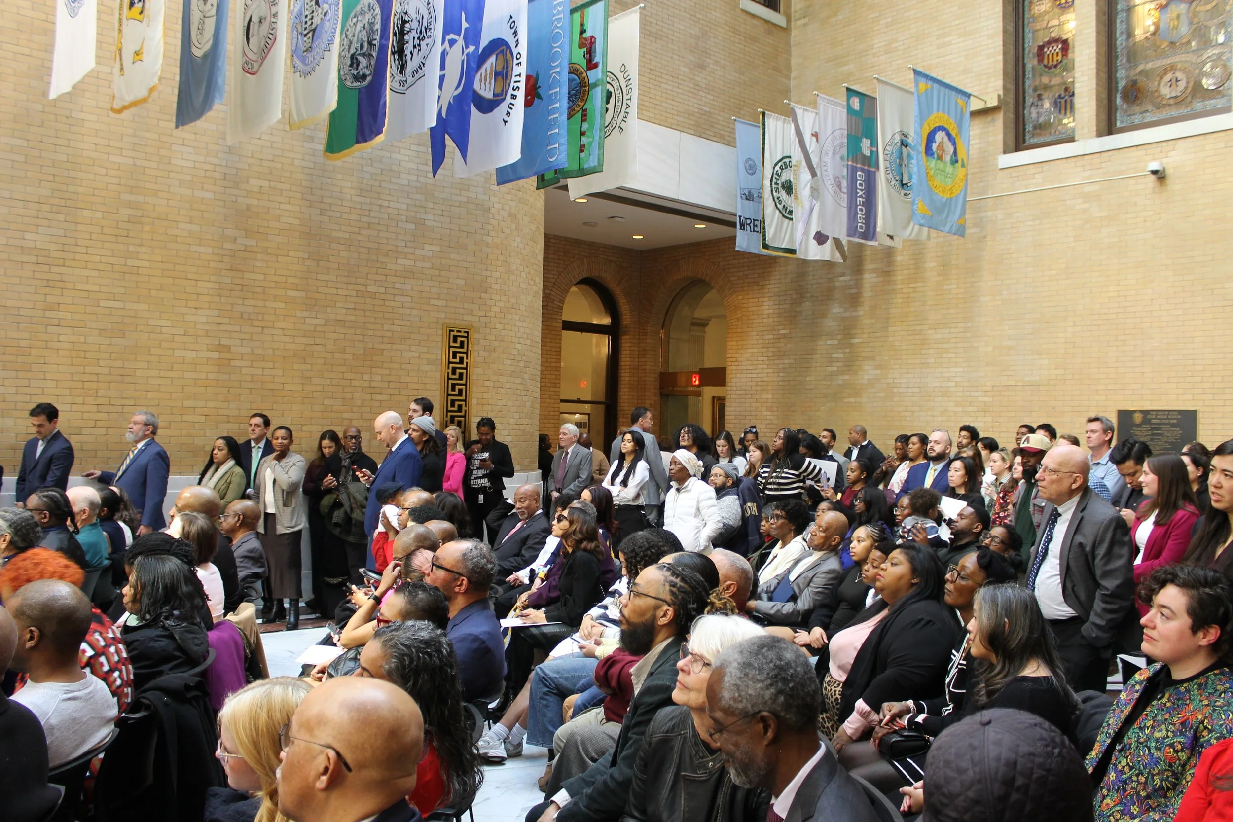 Members of the public and invited guests stand along the walls of the Great Hall of Flags during the event.