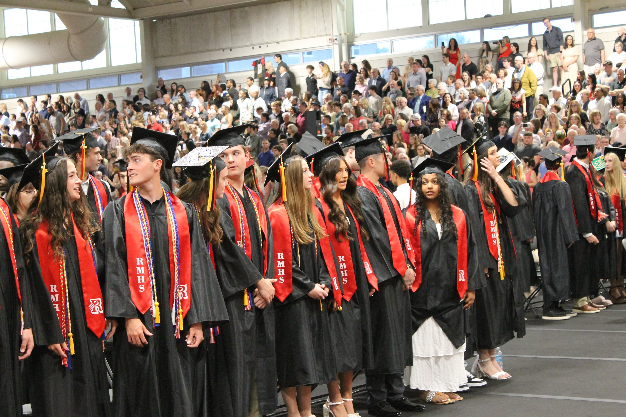 The Class of 2026 stands at attention during the processional as a packed crowd of family and community members fill the stands behind them at the Fieldhouse.