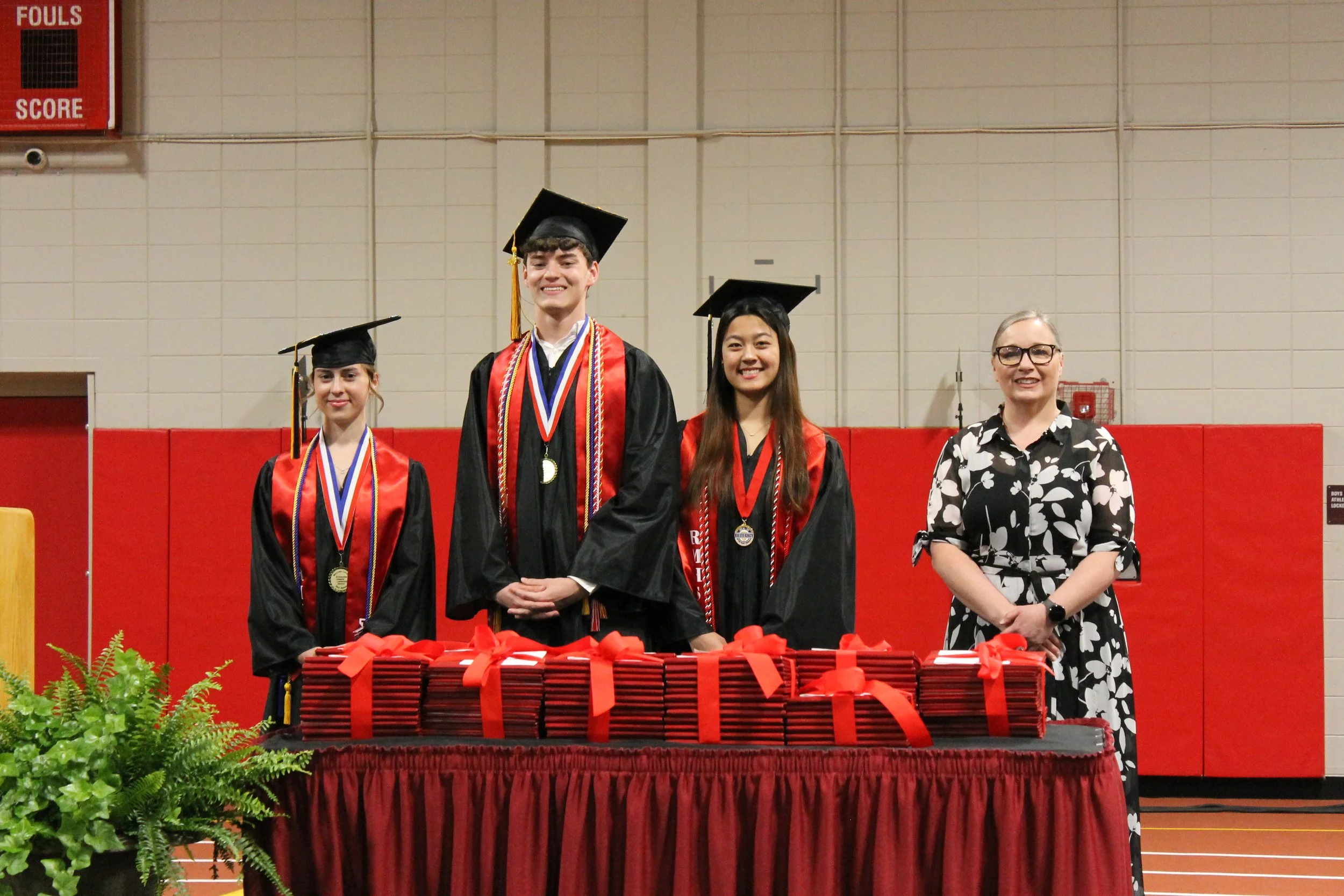 Valedictorian Amelia Barowski, Class President Jason Walsh, and Student Council President Jessica Wong stand with a staff member behind the diplomas,